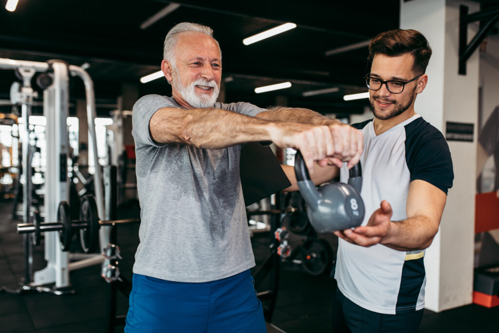 Senior man exercising in gym with his personal trainer.